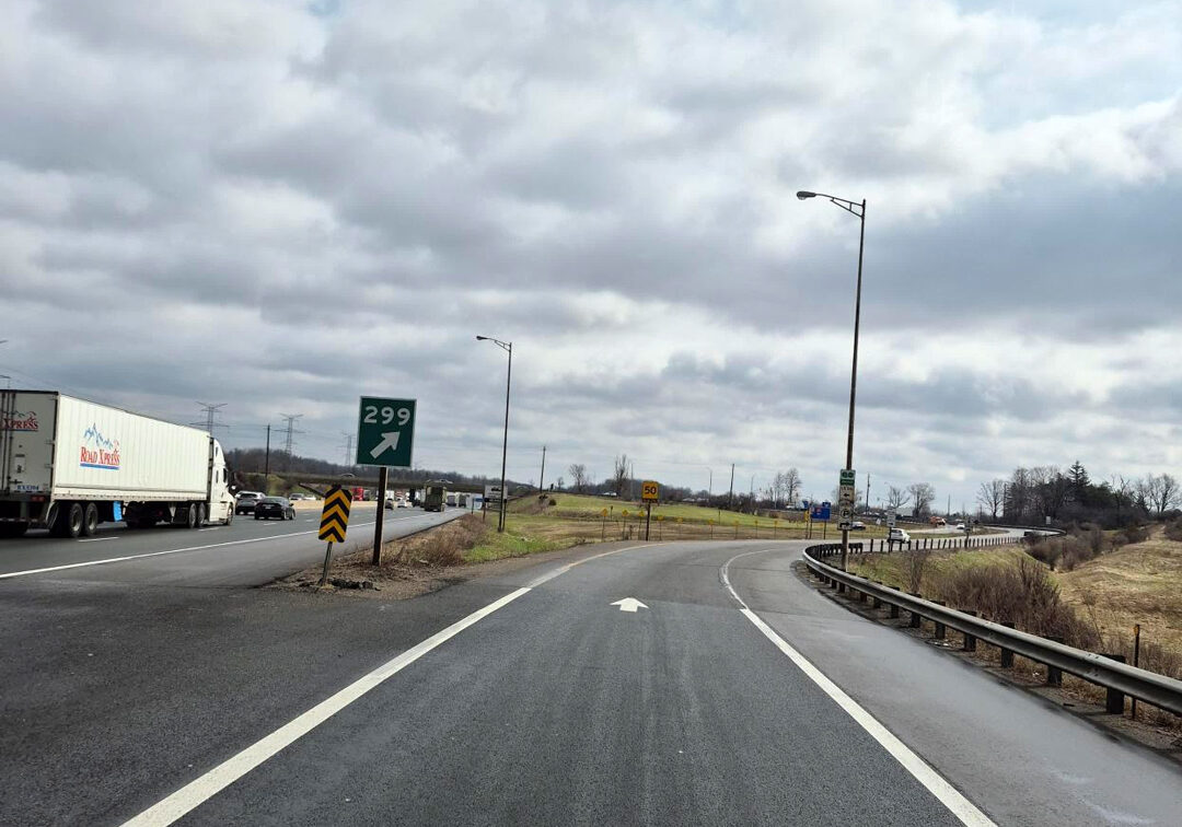 View from a highway ramp showing exit 299, ramp to Brock Road South. Signage, and traffic on Highway 401 also visible.